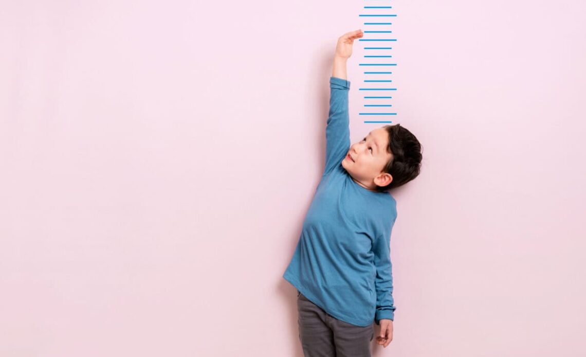 Child measures his height on wall. He is growing taller.