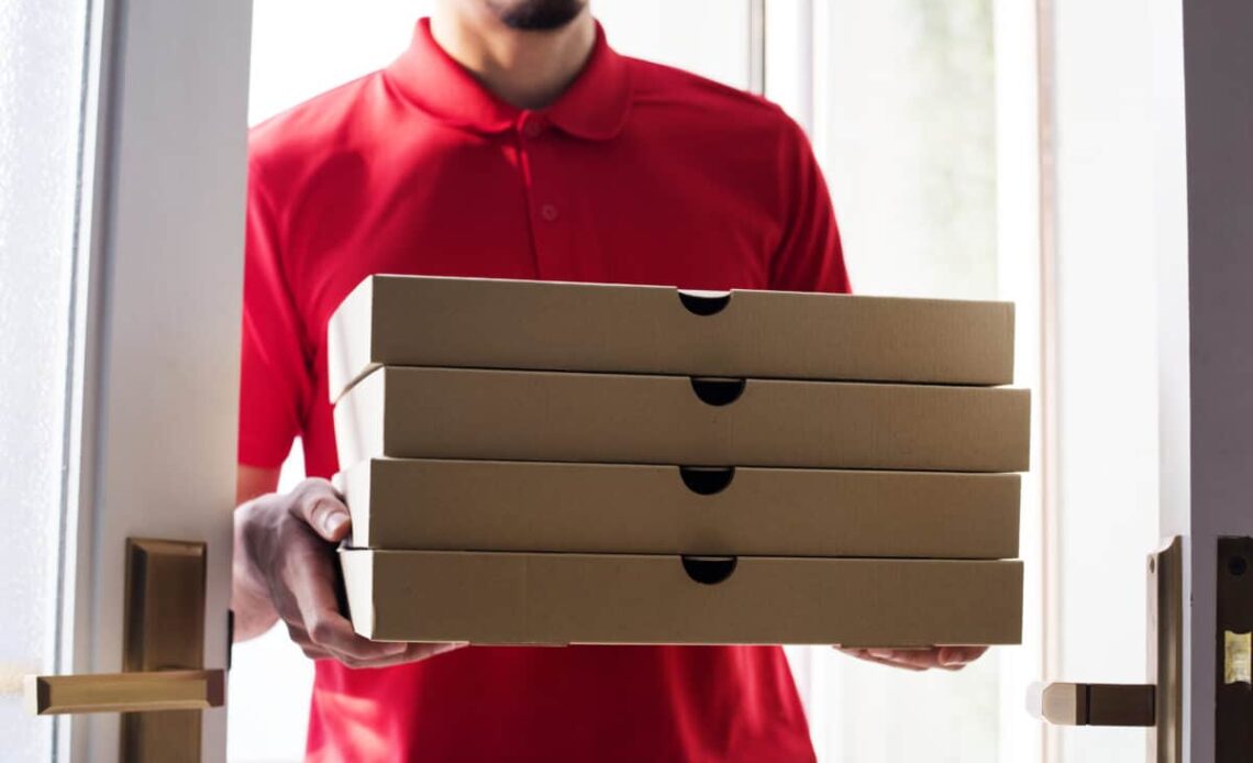 worker carries stack of pizza boxes for delivery